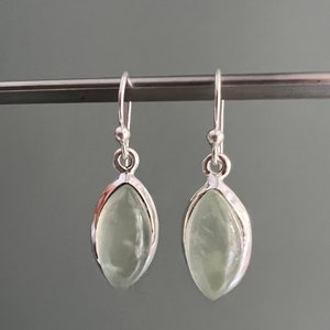 Puede incluir: Un par de pendientes colgantes de plata con piedras ovaladas de color verde claro.