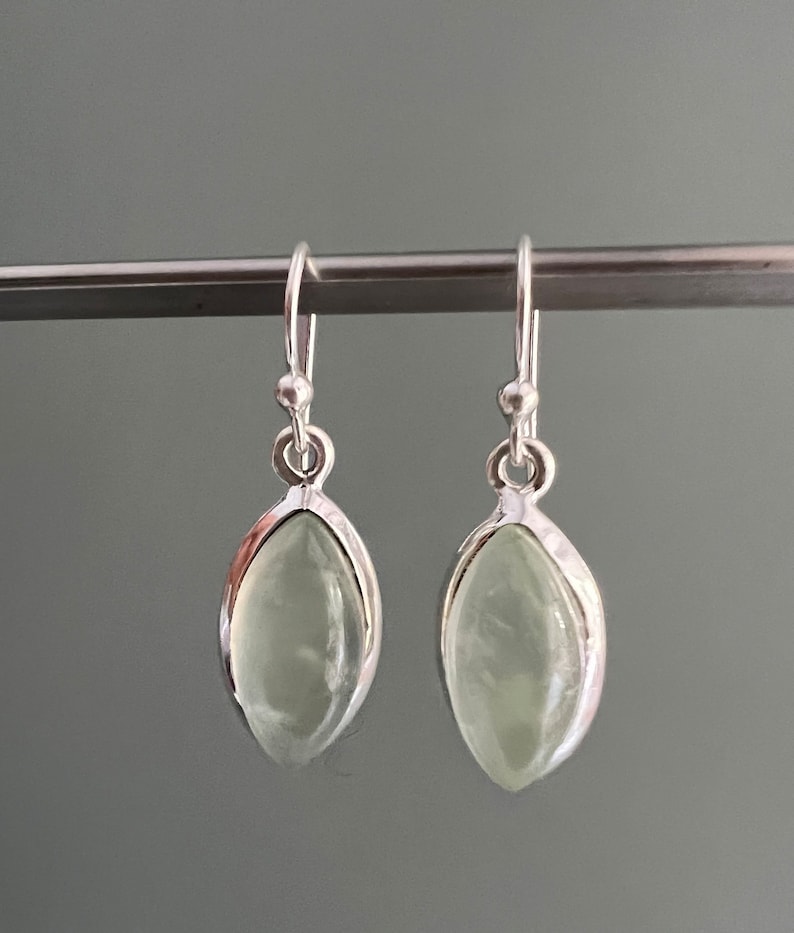 Puede incluir: Un par de pendientes colgantes de plata con piedras ovaladas de color verde claro.