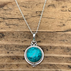 May include: A silver chain necklace with a turquoise stone pendant. The pendant is round and has a silver bezel.