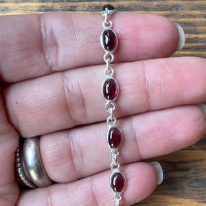 Peut inclure: Un bracelet en argent avec cinq pierres précieuses rouges de forme ovale.