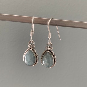 Puede incluir: Un par de pendientes de plata con piedras azul verdosas en forma de lágrima.
