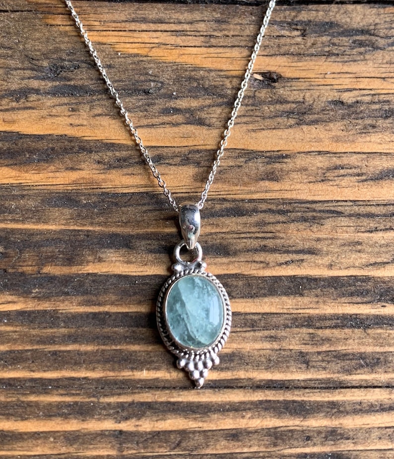 Op de afbeelding: Een zilveren ketting met een lichtblauwe ovale hanger. De hanger is gezet in een zilveren frame met een parelmoerontwerp.