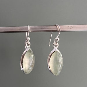 Puede incluir: Un par de pendientes de plata con piedras ovaladas de color verde claro.