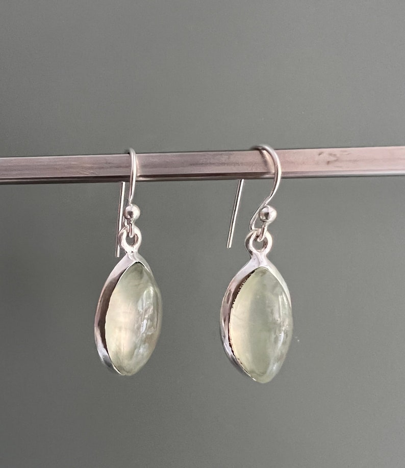 Puede incluir: Un par de pendientes de plata con piedras ovaladas de color verde claro.