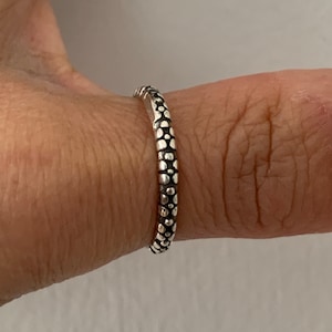 May include: A silver ring with a textured design of small circles. The ring is worn on a finger.