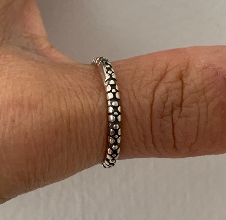 May include: A silver ring with a textured design of small circles. The ring is worn on a finger.