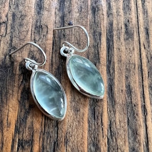 Puede incluir: Un par de pendientes de plata con piedras ovaladas de color verde claro.