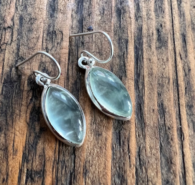 Puede incluir: Un par de pendientes de plata con piedras ovaladas de color verde claro.