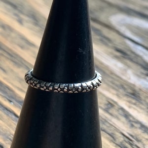 May include: A silver ring with a textured surface. The ring is on a black ring holder.