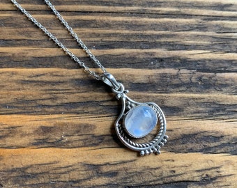 May include: A silver chain necklace with a moonstone pendant. The pendant is set in a silver filigree design.