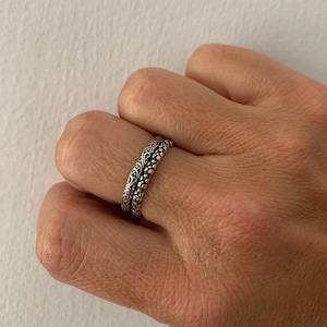 May include: Two silver rings with intricate floral designs. The rings are stacked on top of each other.