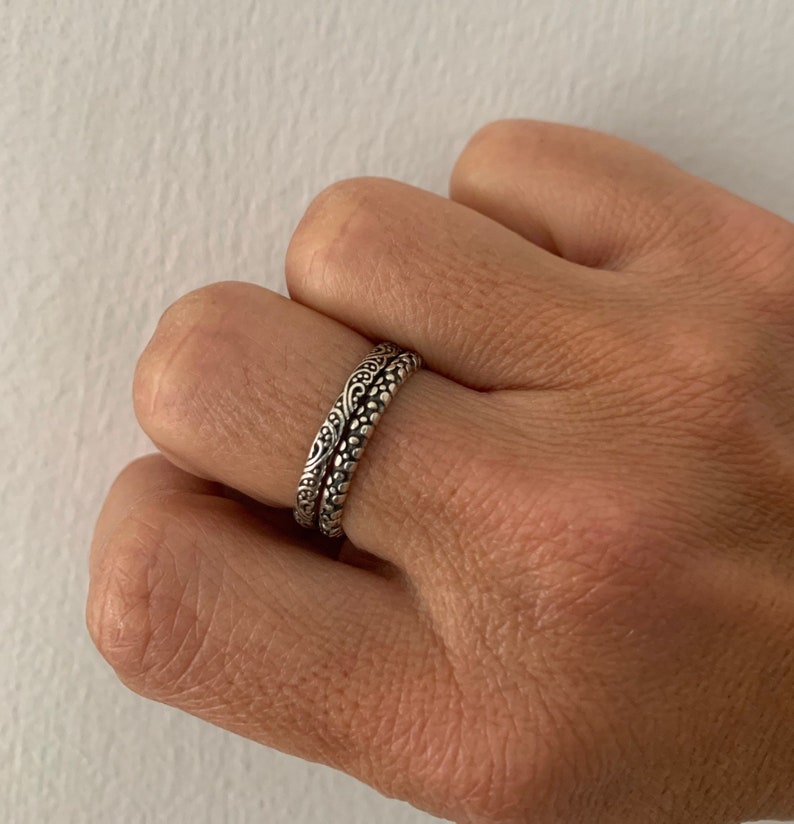 May include: Two silver rings with intricate floral designs. The rings are stacked on top of each other.