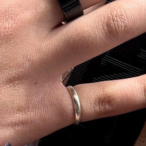 May include: A close-up of a person's hand wearing a silver band ring on their ring finger.