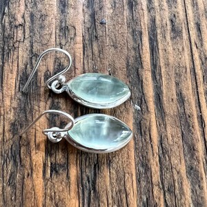Puede incluir: Un par de pendientes de plata con piedras ovaladas de color verde claro. Los pendientes tienen un dise&ntilde;o sencillo y son perfectos para el uso diario.