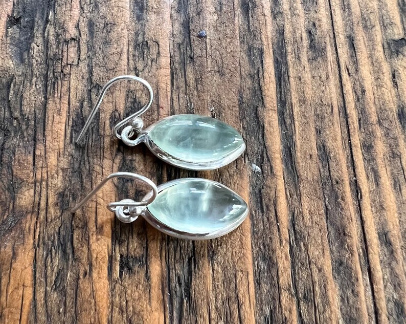 Puede incluir: Un par de pendientes de plata con piedras ovaladas de color verde claro. Los pendientes tienen un dise&ntilde;o sencillo y son perfectos para el uso diario.