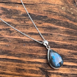 May include: A silver chain necklace with a teardrop-shaped pendant featuring a blue labradorite gemstone.