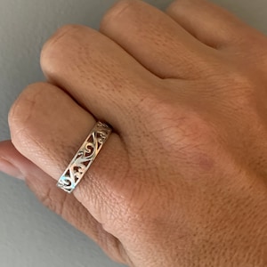 May include: A silver ring with a delicate, intricate design. The ring is made of a thin band with a filigree pattern.