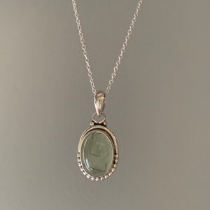 May include: A silver chain necklace with a green stone pendant. The pendant is oval shaped and has a silver border.