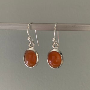 Puede incluir: Un par de pendientes de plata con piedras ovaladas de color naranja.