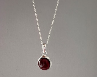 May include: A silver chain necklace with a round pendant featuring a dark red gemstone.