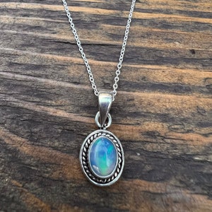 May include: A silver chain necklace with a silver pendant featuring a round opal gemstone.