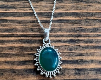 May include: A silver chain necklace with a green oval gemstone pendant. The pendant is surrounded by a silver filigree design.