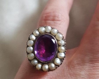 May include: A silver ring with a large purple gemstone surrounded by a halo of white pearls.
