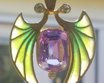 May include: A gold pendant with a large, faceted, purple gemstone surrounded by two wings with green and white enamel. The pendant is on a gold chain.
