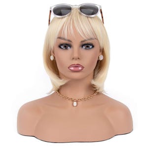 May include: A mannequin head with a blonde wig, sunglasses, gold necklace with a pearl pendant, and matching earrings. The mannequin has full makeup and is set against a white background.
