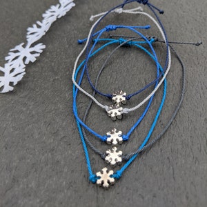 Può includere: Quattro braccialetti con ciondoli a forma di fiocco di neve argentati. I braccialetti sono realizzati in cordoncino blu, grigio e bianco.