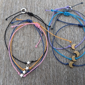 May include: Five colourful friendship bracelets with silver star and gold crescent moon charms. The bracelets are made of thin, braided cords.