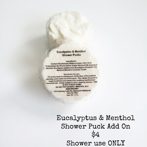 May include: Two white shower pucks with the text "Eucalyptus & Menthol Shower Pucks" and a list of ingredients and directions for use. The text "Eucalyptus & Menthol Shower Puck Add On $4 Shower use ONLY" is below the image of the pucks.