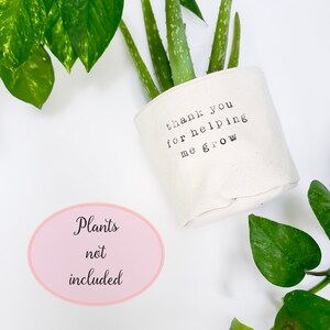 May include: White fabric pot with the text "thank you for helping me grow" printed on it. A green aloe vera plant is in the pot. The text "Plants not included" is written on a pink oval sticker.