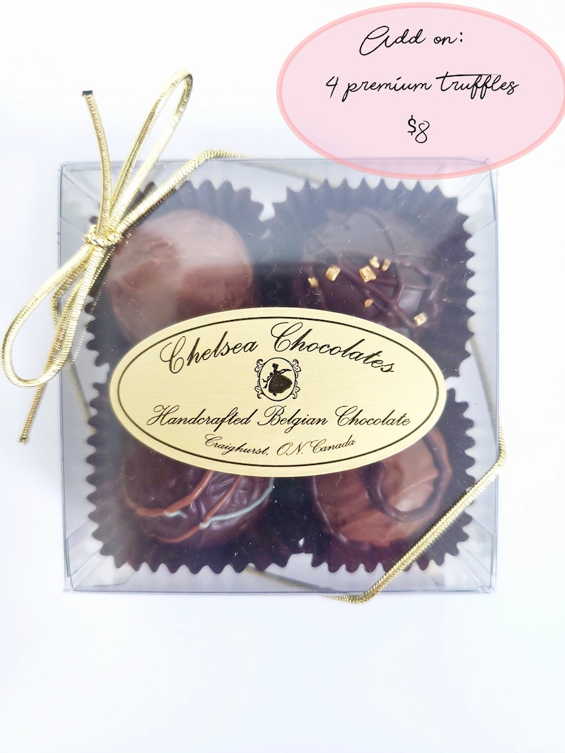 May include: A clear box with a gold ribbon tied around it. Inside the box are four chocolate truffles. The box has a label that says "Chelsea Chocolates" and "Handcrafted Belgian Chocolate".