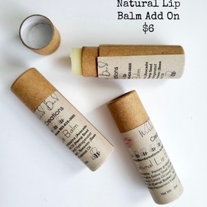 May include: Two brown cardboard tubes of natural lip balm with a white label and black text. The label reads "Bend Creations Lip Balm" and lists the ingredients. The text "Natural Lip Balm Add On $6" is printed in black on a white background.