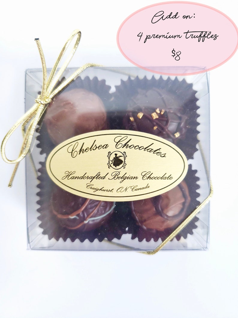 May include: A clear box with a gold ribbon tied around it. Inside the box are four chocolate truffles. The box has a label that says "Chelsea Chocolates" and "Handcrafted Belgian Chocolate".