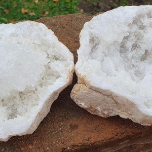 May include: Two white crystal geode halves with a rough exterior and a smooth, white, crystalline interior.