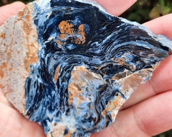 May include: A blue and gold tiger's eye stone with a swirling pattern. The stone is rough and has a natural, unpolished finish.