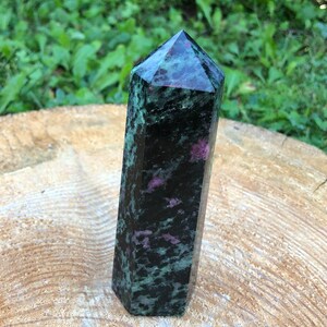 May include: A dark green and black crystal point with pink and white inclusions. The crystal is polished and has a pointed tip.