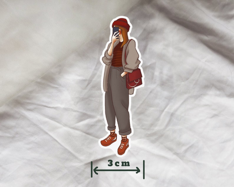 May include: A sticker of a person wearing a red hat, a striped sweater, and brown pants. The person is holding a phone and a brown bag with a circular handle. The sticker is 3 inches wide.