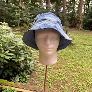 Op de afbeelding: Een denim bucket hat met een patchwork design. De hoed is gemaakt van verschillende tinten blauwe denim, waardoor een textuur en unieke uitstraling ontstaat. De rand is effen blauw. De hoed wordt getoond op een mannequinhoofd.