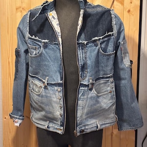 Peut inclure: Veste en jean patchwork avec fermeture éclair et boutons. La veste présente différentes nuances de denim bleu, avec des coutures et des détails de poche visibles. L'intérieur est doublé d'un motif. La veste est présentée sur un mannequin.