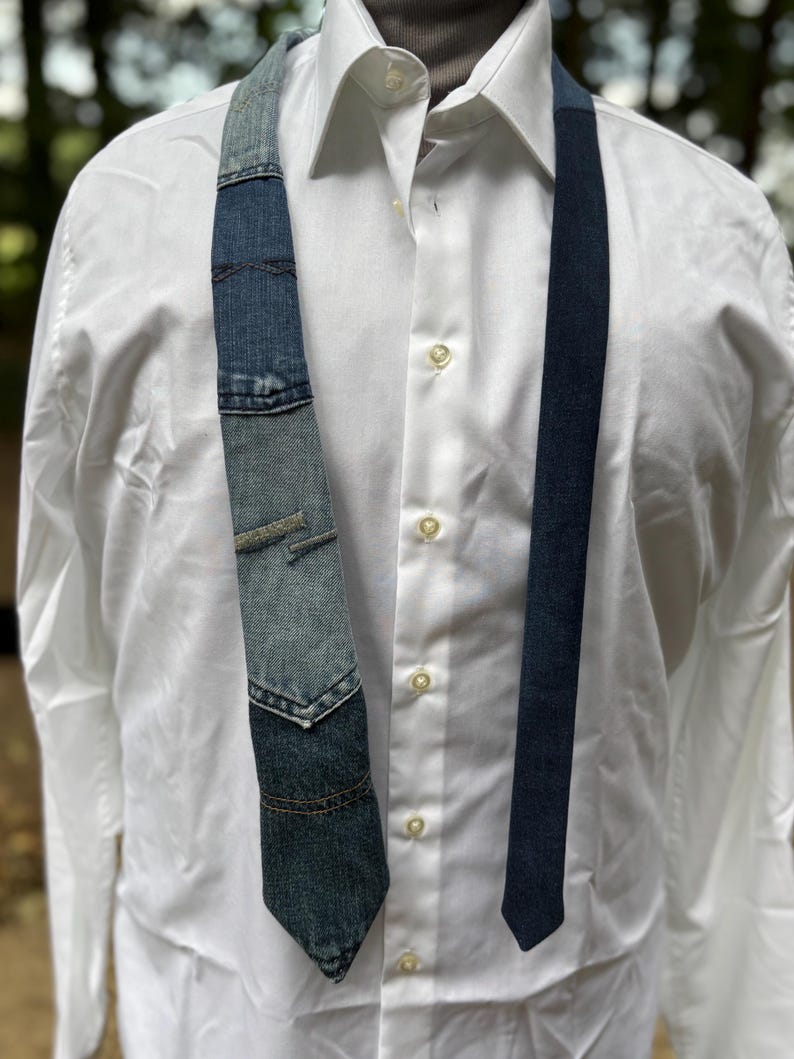 May include: A denim tie with a patchwork design, featuring various shades of blue denim. The tie is paired with a white dress shirt. The tie's design includes pocket details and contrasting stitching, adding a unique, handcrafted touch to the accessory.