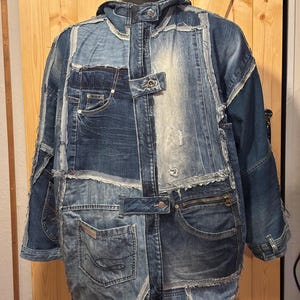 Peut inclure: Veste en jean patchwork dans diverses nuances de bleu. La veste présente de multiples patchs en denim, des poches et une fermeture éclair. Le design comprend une capuche et des boutons, créant un aspect unique et texturé. La veste est présentée sur un mannequin.