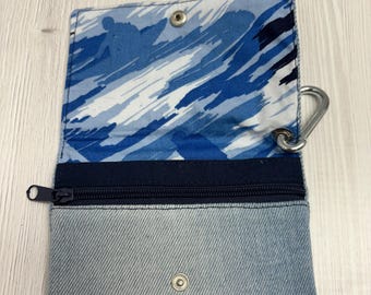 May include: A small blue denim pouch with a zipper closure and a blue and white patterned lining. The pouch has a metal snap closure and a carabiner clip.