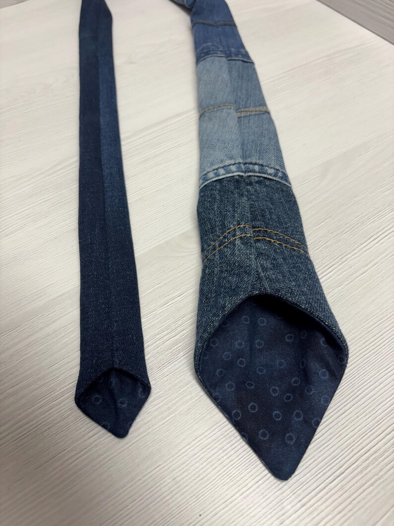 May include: A denim tie with a patchwork design, featuring various shades of blue denim. The tie's interior lining has a dark blue pattern with small circles. The tie is a classic accessory.