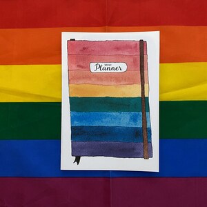 Puede incluir: Una ilustración de acuarela de un planificador semanal de colores arcoíris con el texto "Weekly Planner" en la portada.