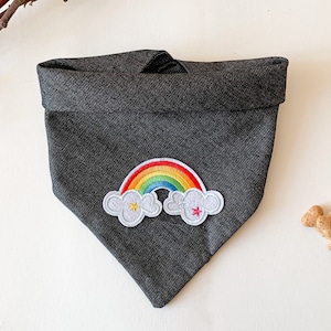 May include: A dark grey fabric dog bandana with a rainbow and cloud applique. The applique has a yellow star in one cloud and a pink star in the other cloud.