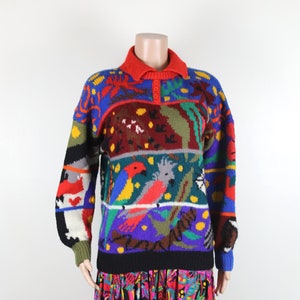 May include: A colorful knitted sweater with a multi-colored parrot design. The sweater has a red collar and a black band at the bottom.