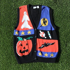 Pu&ograve; includere: Un gilet di maglia nero, rosso, blu e bianco a tema Halloween. Il gilet presenta un fantasma, un pipistrello, una zucca, bastoncini di zucchero e una strega su una scopa.